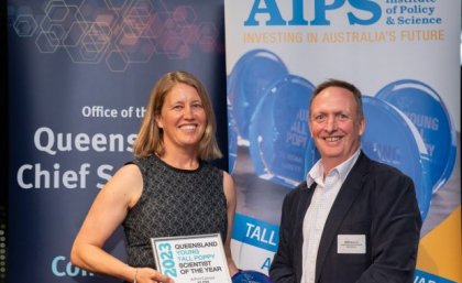 Associate Professor Carissa Klein with Jamie Merrick, Director-General, Department of Environment and Science. Two people stand smiling in front of banners at an awards night, one of them is holding an award.